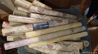Multiple sealed rolls of floral and vine pattern wallpaper packed in a container.