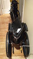 Side view of two folded manual wheelchairs stacked together showing black frames and padded seats.