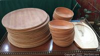 Stack of round wooden plates, several wooden bowls, and one carved elongated wooden tray, all placed on a wooden surface.
