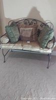 Front view of metal bench with cushions and pillows on carpeted floor.
