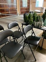 Set of four black folding chairs arranged in cluster near other items indoors, showing overall appearance and condition.