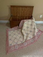 Open wooden cedar chest with natural finish. Rug partially draped over the front edge of the chest revealing both items.