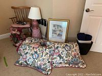 Overall view of chair, lamp, framed picture, comforter set pillows, faux flowers, and basket trash cans