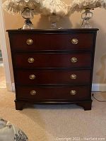 Front view of a dark wooden chest of drawers with four drawers and metal handles, placed on carpet.