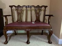 Front view of wooden bench with carved backrest and burgundy vinyl upholstered seat.