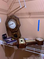 Photo showing two wooden wall clocks, one with octagonal face and another elongated rectangular clock, along with papers and CD on the shelf.