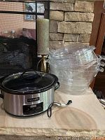 Full lot showing Crockpot, stacked clear plastic serving trays, large candle on metal stand, and laying base surface.