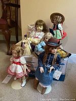 Wide view showing eight assorted dolls in various costumes and hair styles, arranged on a box and floor.