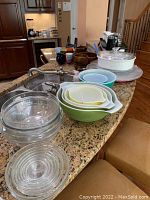 Clear glass mixing bowls with concentric circle design stacked on countertop, nested vintage Pyrex bowls in multiple colors also visible.