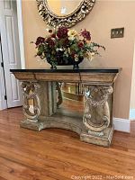 Front view of ornate foyer table with faux flowers on top against wall with mirror