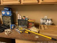 Wide view of countertop with assorted tools, two organizer shelves filled with screws and bolts, fire starter logs, grout, and a yellow extendable tool.