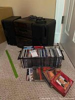 Photo showing JVC stereo system with wire basket filled with CDs and tapes, some CDs and tapes placed on floor in front.