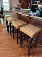 Four padded bar stools lined up along a kitchen counter, showing seats and legs.