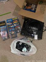 Photo shows Pioneer Elite Blu-ray player with cables and remote controls, a box of Blu-ray movies, and a plastic bag of Vetch phones on carpeted floor.