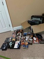 Photo showing multiple assorted DVDs and VHS tapes laid out on floor near boxes.