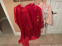 Three robes hanging on hangers: two red silk with embroidery and one pink polyester.