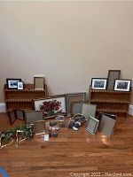 Wider view of two wooden spoon shelves on floor with multiple picture frames and decorative items arranged in front.