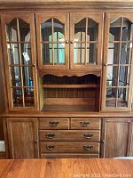 Front view of the wooden china cabinet showing glass panel doors on upper section, four drawers, two cabinets below, and open middle shelf area.