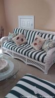 Front view of white wicker couch with green and white striped cushions and decorative pillows.