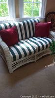 Front view of white wicker loveseat with green and white striped cushions and two red pillows, showing overall condition and styling.