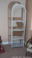 Full view of tall white wicker shelving unit standing on carpeted floor against wall.