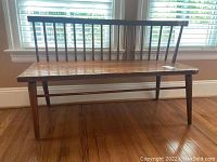 Front view of wooden bench showing curved backrest made of thin vertical spindles and solid flat seat.