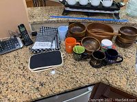 All items on granite kitchen counter showing wooden salad bowls, serving bowl and tongs, coffee cups, oven mitt, dish towels, Panasonic Bluetooth phone system with two handsets and base station.