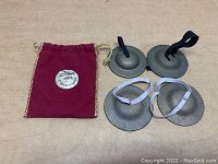 Two sets of four finger cymbals: two with black straps, two with white straps, accompanied by red Zildjian logo carrying pouch, laid on a flat surface.
