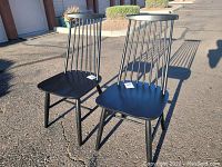 Front angled view of two black wooden chairs outdoors showing spindled backs and flat seats.