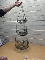 3 tier black metal hanging basket held up by hand showing all tiers and top hook.