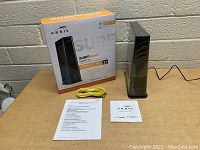 Front view of retail box, modem/router standing upright, Ethernet cable and documentation laid out