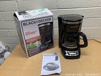 Black & Decker coffee maker with box and manual on a wooden surface against a brick wall.