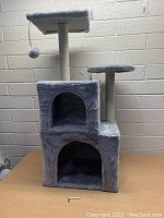 Front view of grey cat tree showing two cubby holes, two platforms, and one scratching post with hanging ball toy.