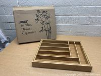 Photo of the bamboo drawer organizer next to its box showing the product name 'Premium Bamboo Drawer Organizer'.