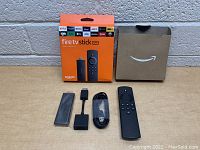 Amazon Fire TV Stick Lite with original packaging, remote, HDMI extender, power adapter, and USB cable.