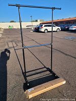 Black metal garment rack standing outdoors on asphalt, with packaging box placed in front.