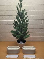 Large green faux pine-style tree in white pot with two Threshold brand candles in white ceramic containers with four wicks each, labeled Clove & Black Currant scent.