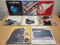 Eight vinyl records displayed on a table with visible album covers including Jeff Beck Wired, The Beatles 1967-1970, Aerosmith, Pat Benatar, Mose Allison, John Williams, Rickie Lee Jones.