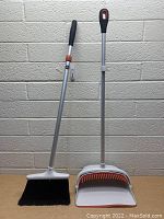 Front view of OXO broom and dust pan with ergonomic handle grips and silver handles.