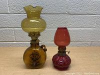 Photo of two vintage glass hurricane lamps, one amber with round base and ruffled cracked chimney, one red with textured swirl pattern base and smaller chimney.