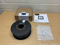 Overview of grey PETG 3D printer filament spool, silica gel moisture pack, instruction sheet, and box on wooden surface.