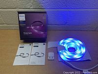 Photo of Philips Hue Shape Light RGB lightstrip lit in blue color with box, manuals and connector visible.