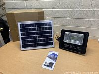 Photo showing new solar LED flood light, solar panel, and instruction manual on table.