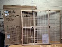 ToddleRoo Extra-Wide Wire Mesh Gate in white metal frame leaning against wall with original packaging. Clear printed box with product specifications visible.