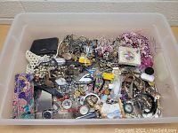 Plastic tub filled with assorted jewelry items including beaded necklaces, watches, keychains, and small cases.