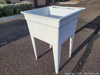 Front left angle view of a white plastic utility sink with four legs on an outdoor paved surface