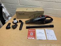 Photo showing VacLife cordless handheld vacuum, attachments, filter, charger, user manuals, and original box on wooden table against a grey brick wall