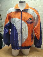 Front full view of vintage 1995 Phoenix All-Star Game jacket in size medium, showing vibrant orange, purple, and white nylon construction with embroidered logo on chest.