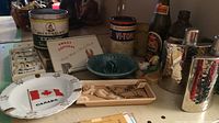 Full view of assorted vintage tobacco tins, ashtrays, labels, and small figurines arranged on a shelf