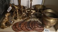 Photo showing several polished brass candleholders, a brass dog figurine, brass elephant figurine, set of five embossed circular brass wall medallions, and round brass tray.